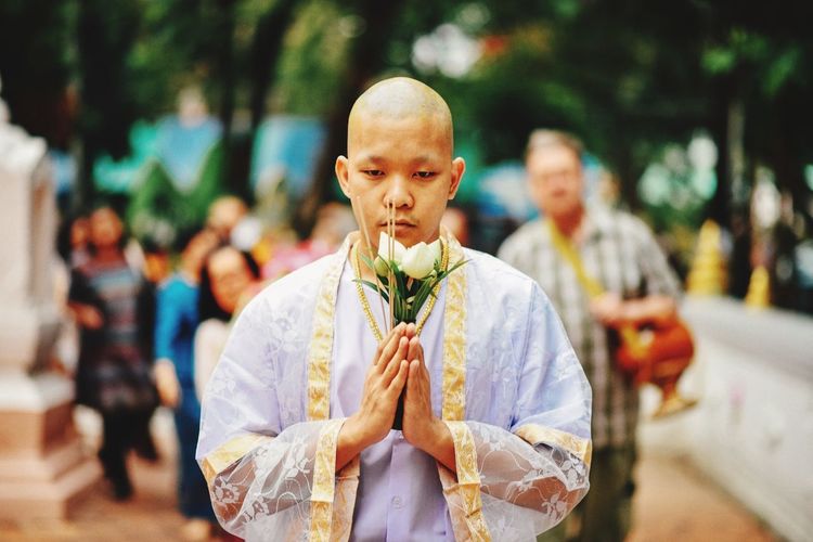 Portrait of monk holding flowers while praying