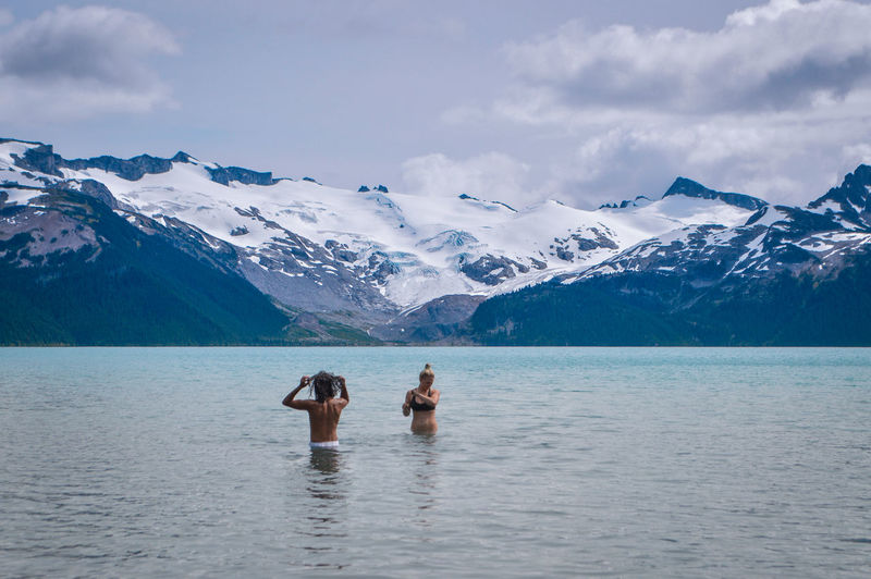 Friends swimming in lake against snowcapped mountains