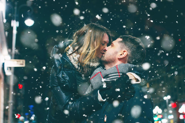 Couple romancing while standing against sky at night during snowing