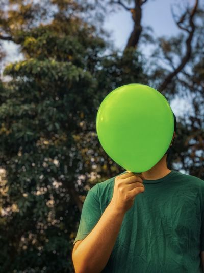 Cropped image of man holding green balloon against trees.