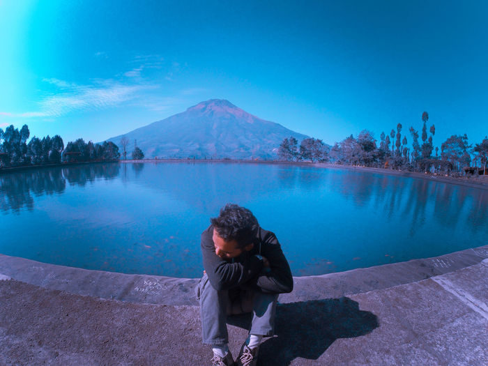 High angle view of man sitting by lake against mountain and sky