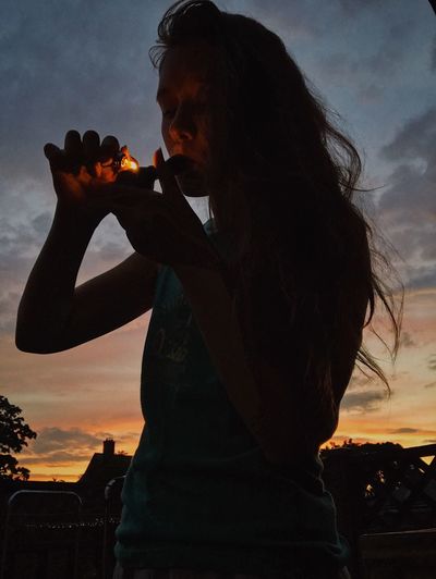 Side view of young woman drinking beer at sunset
