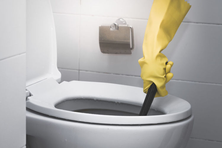 Cropped hand of person wearing yellow protective glove while washing toilet bowl