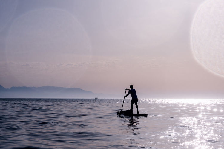 Silhouette of man playing stand up paddle. paddling in the sea at dawn.