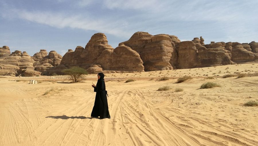 Side view of woman in burka standing on desert during sunny day