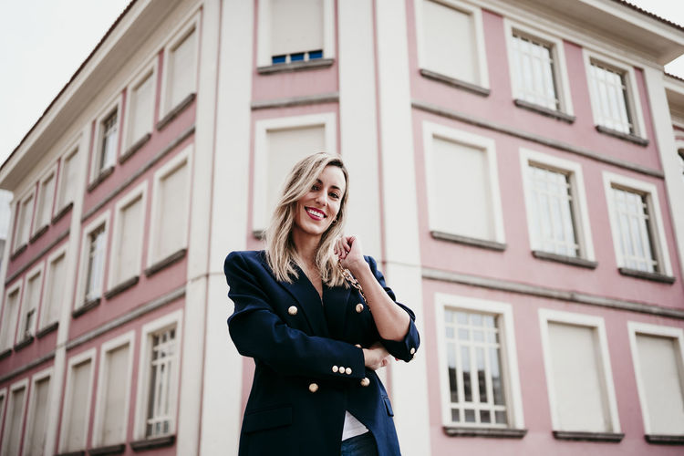 Smiling beautiful woman standing against building in city