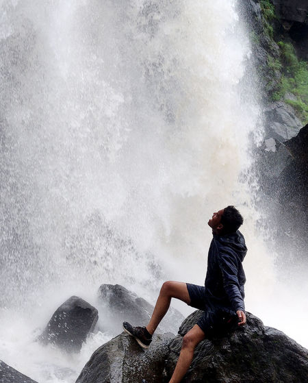 Man sitting on rock by waterfall