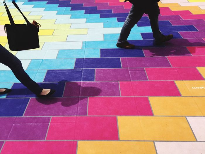 Low section of people walking on multi colored pattern floor