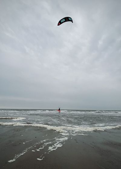 Person paragliding on beach against sky