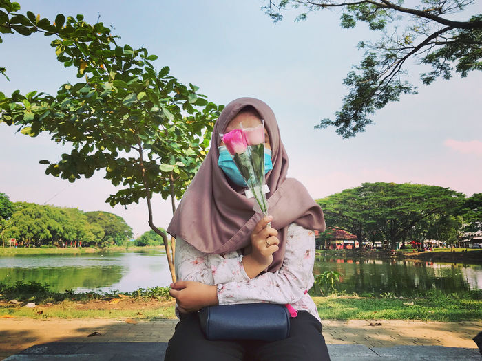 Full length of woman wearing hijab against lake against sky girlfriend take a flower