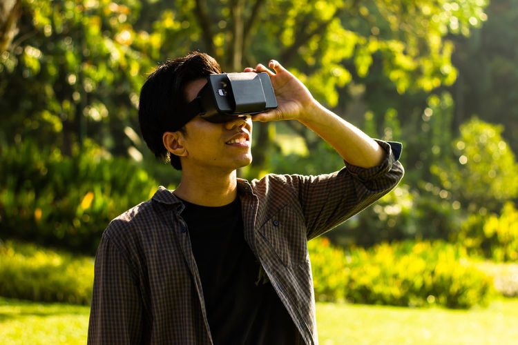 Young man looking through virtual reality while standing at park