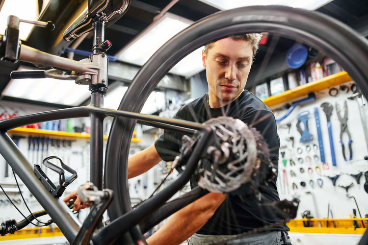 Male technician attaching wheel to bike while working in professional modern workshop