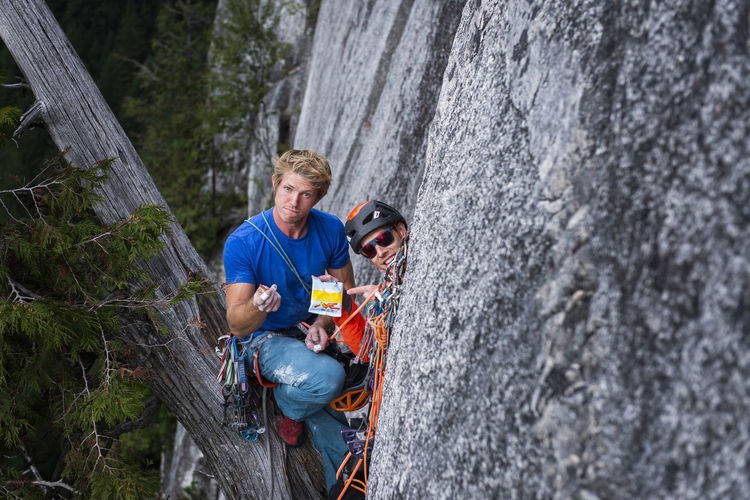 Two climbers looking funny at camera with candies while rock climbing