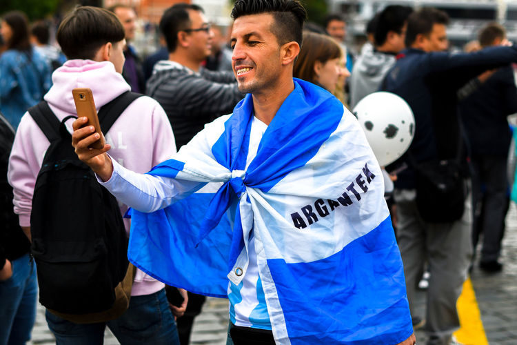 Man wearing argentinian flag while taking selfie outdoors