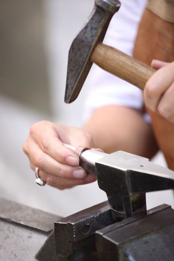 Midsection of person hammering metal in workshop