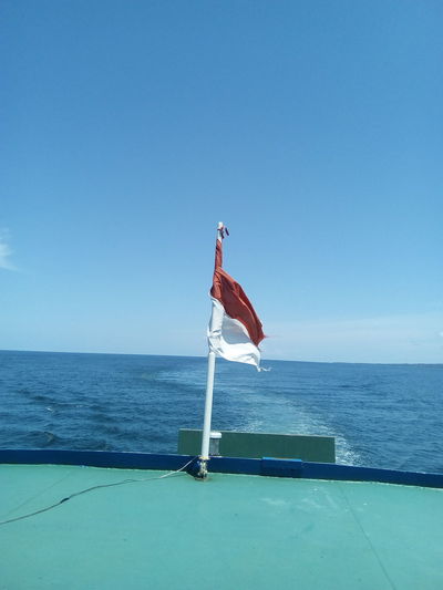 Indonesian flag on boat sailing in sea against blue sky