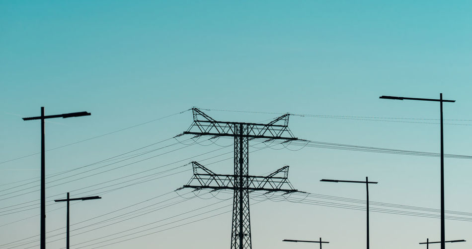 Low angle view of silhouette electricity pylon against clear sky