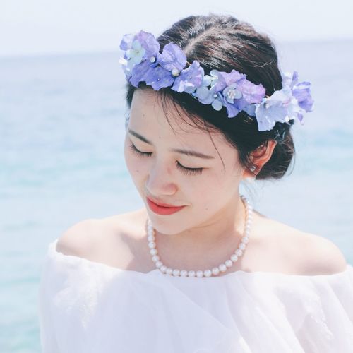 Close-up of young woman wearing artificial flowers against sea