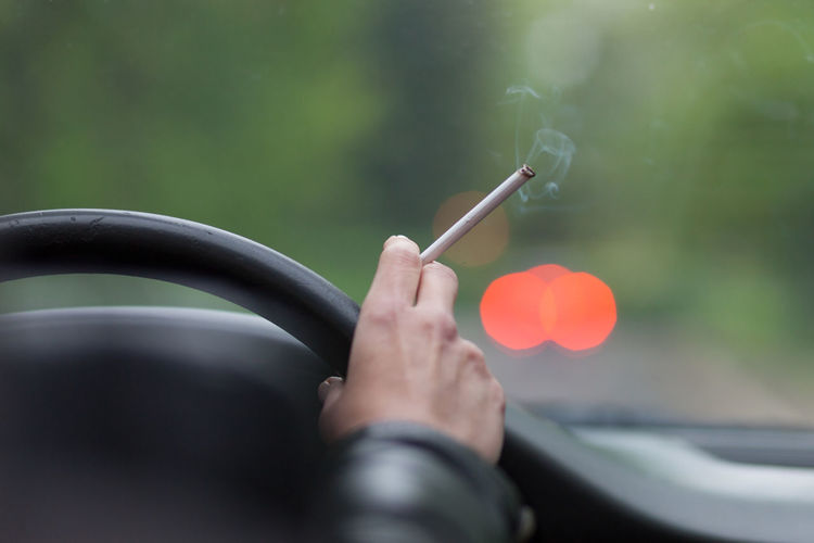 Cropped hand of woman holding cigarette in car
