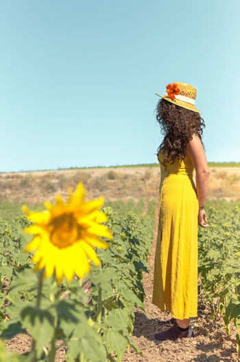 Woman standing on sunflower field against clear sky