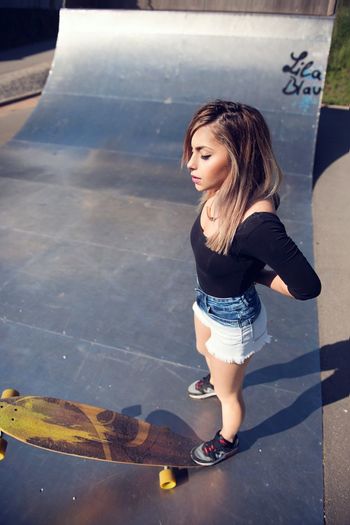 Full length of young woman standing by skateboard