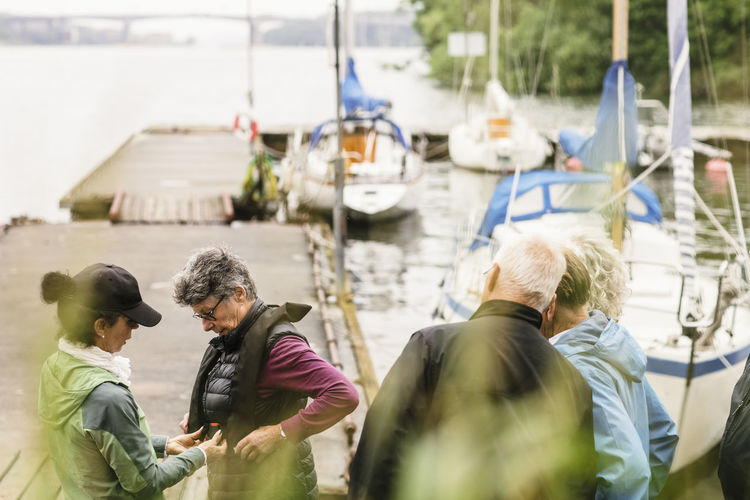 Female instructor helping senior men and woman about life jacket during boat master course