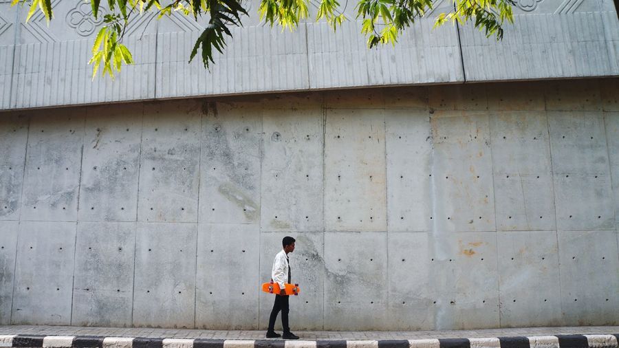 Full length of boy walking on footpath against wall
