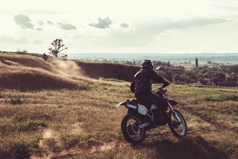 Rear view of man riding motorcycle on field against sky