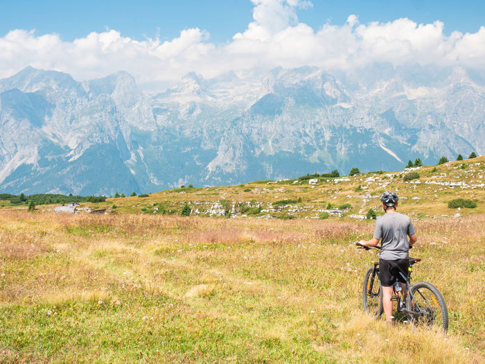 Young man in safety helmet sitting on bicycle and looking at misty mountains over dolomite valley