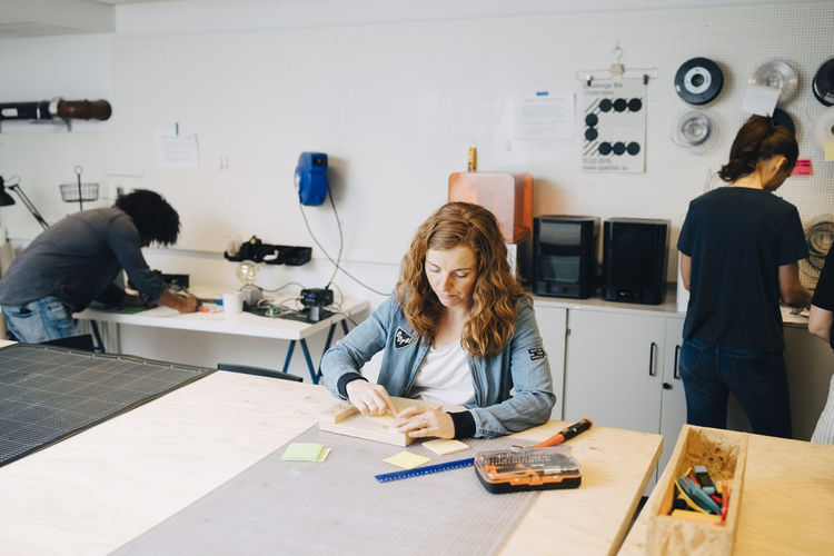 Confident female technician working on wood at workbench with colleagues in office