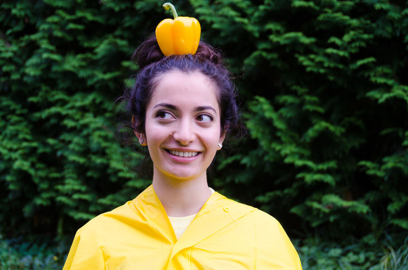 Close-up of smiling young woman with yellow bell pepper on head