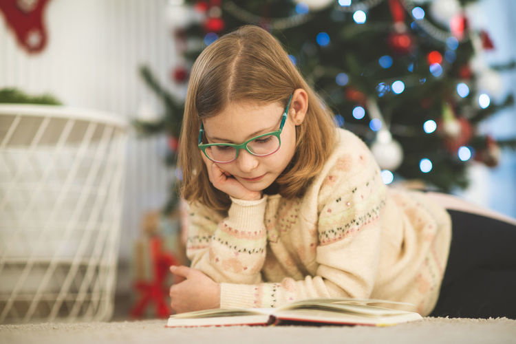 Girl reading book while lying at home during christmas
