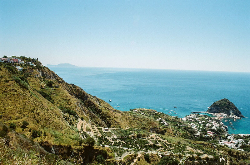 Scenic view of mountain by sea against clear blue sky