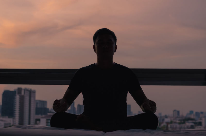 Mindful healthy mature asian man practicing meditation at home sitting on bed.