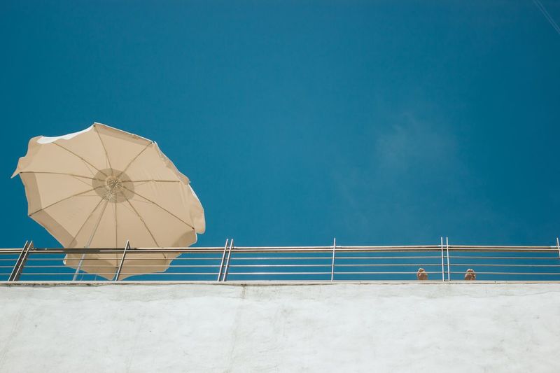 Low angle view of parasol by railing against clear blue sky