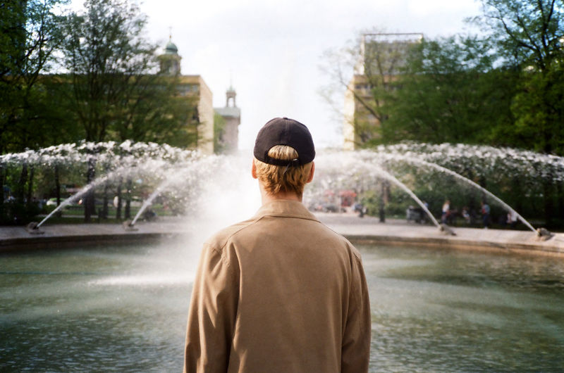 Rear view of man standing by fountain against trees