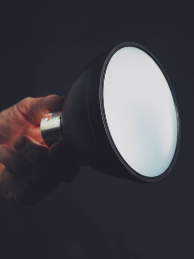 Close-up of hand holding illuminated lamp against black background