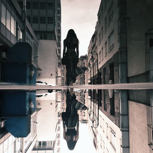 Rear view of woman reflecting on puddle amidst buildings in city