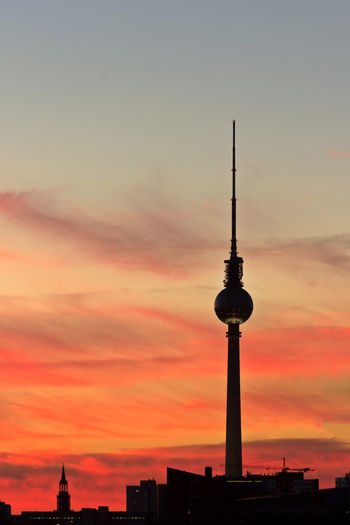 Silhouette of communications tower in city during sunset
