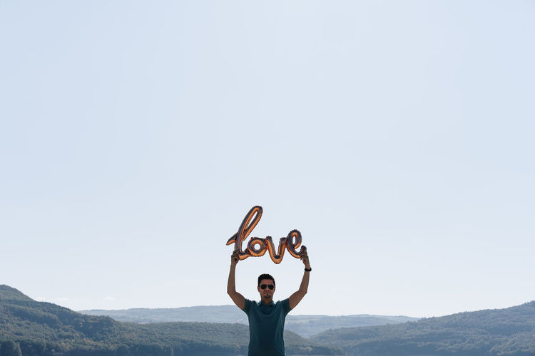 Man holding love text balloon standing against clear sky
