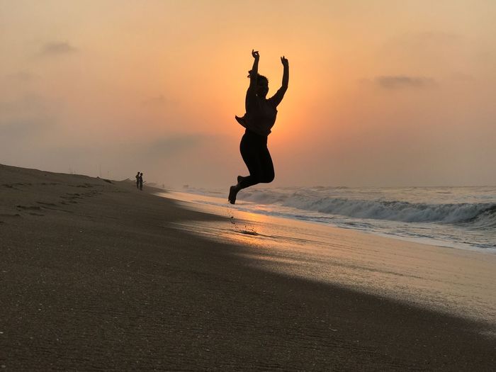Full length of woman jumping on beach during sunset