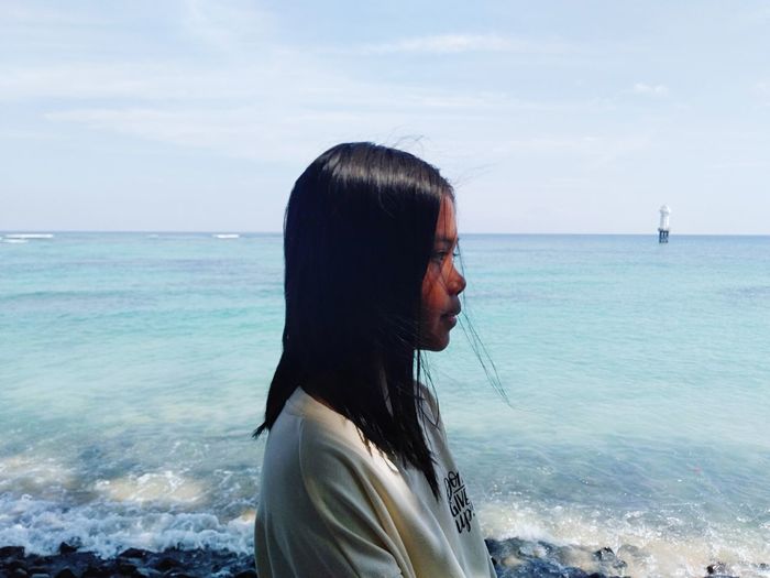 Side view of girl standing by sea against sky