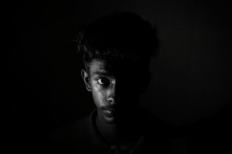 Young man looking away while standing against black background