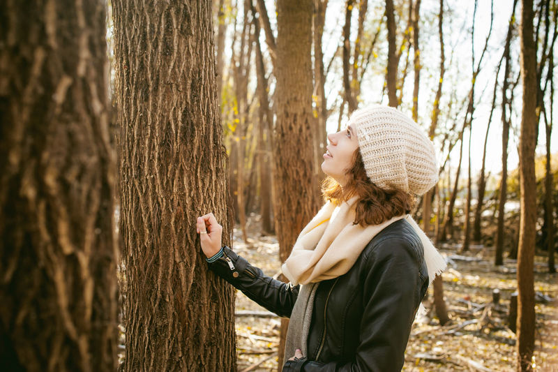 Side view of young woman standing by tree in forest