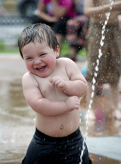 Little boy playing in an urban fountain, happy to be cooling off on a hot day