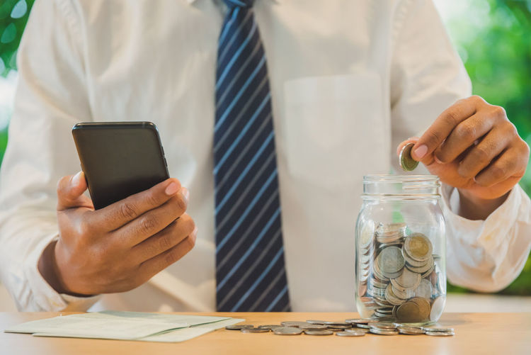 Midsection of man holding smart phone in jar on table