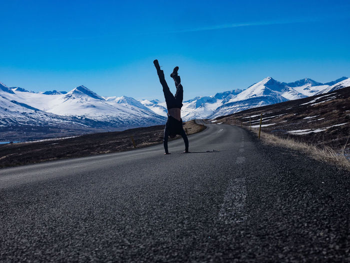 Full length of man doing handstand on road against snowcapped mountains