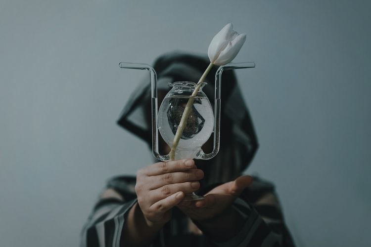 Person wearing raincoat while holding tulip against gray background