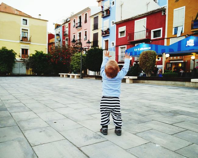 Rear view of preschool boy playing on sidewalk in city