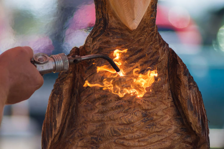 Cropped image of man using blow torch on wooden sculpture
